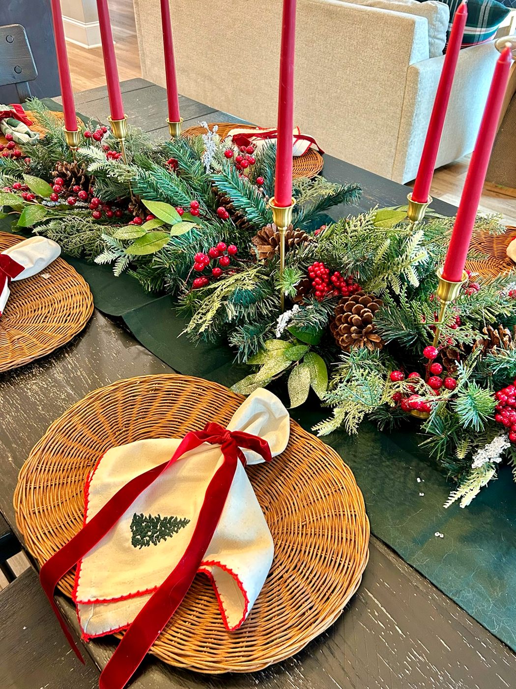 A holiday place setting with a ribboned napkin, greenery, berries, and red taper candles
