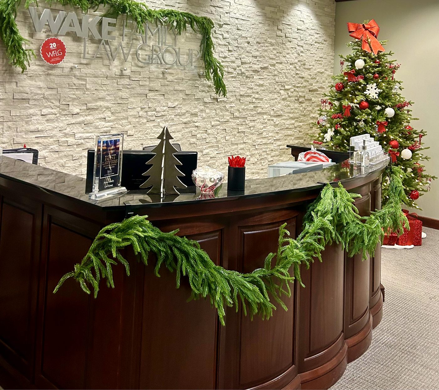 An office reception desk draped with fresh garland, with a decorated tree in the corner